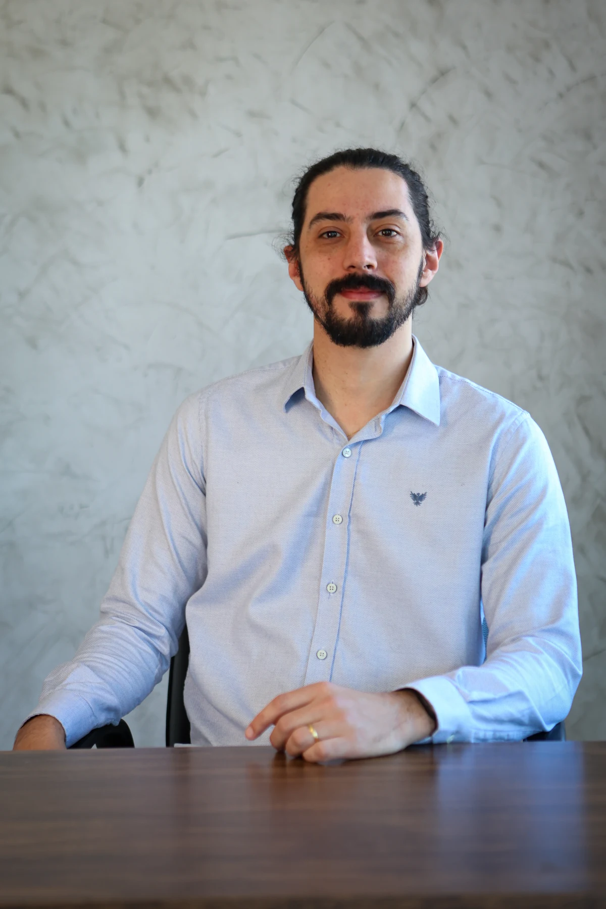 Tiago Galves de camisa azul-clara, sentado à mesa, com expressão tranquila e olhar direto